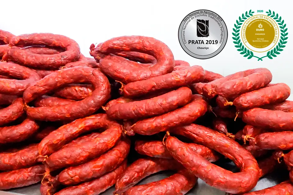 Pile généreuse de Chouriços portugais artisanaux traditionnels Extra 220 g de Quintinha d'Aldeia présentés en étal, accompagnés en haut à droite des macarons de médailles d'argent 2019 et d'or 2020 et 2024 du concours national.