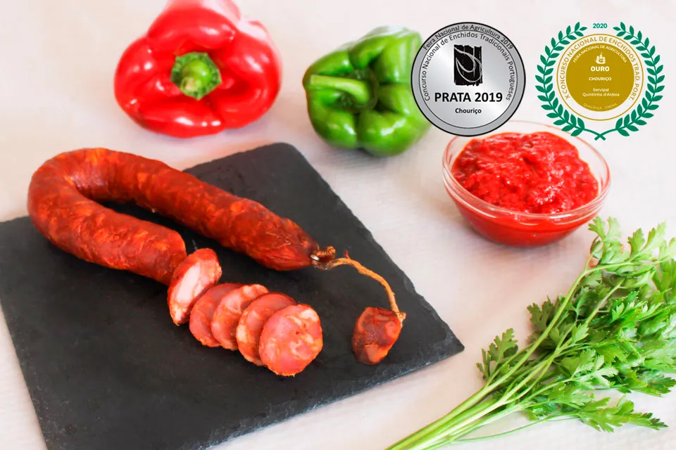Chouriço portugais artisanal traditionnel Extra 220 g de Quintinha d'Aldeia tranché sur une ardoise, accompagné de poivrons, persil frais et pâte de poivron, mis en valeur avec ses médailles aux concours nationaux : médaille d'argent 2019 et médailles d'or 2020 et 2024.