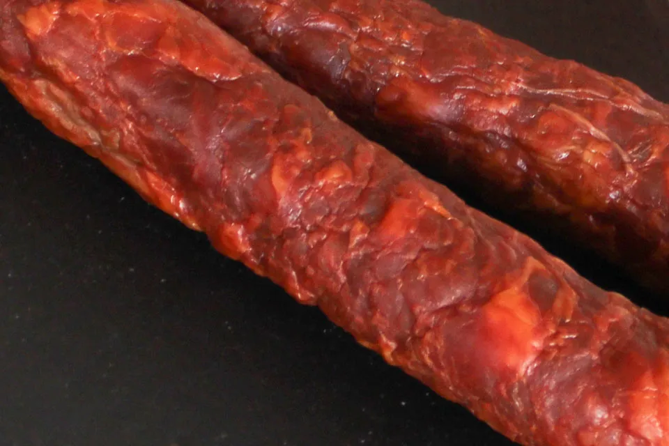 Gros plan détaillé sur la texture fumée et pimentée de deux Chouriços portugais artisanaux piquants 220 g de Quintinha d'Aldeia, révélant le grain fin de la viande et le fumage traditionnel.