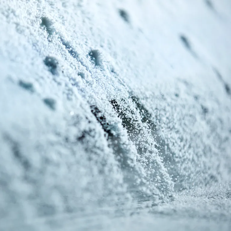 Plan macro très rapproché montrant la texture fine et délicate de grains de sel marin naturellement cristallisés dans les salines Necton. Les fins cristaux blancs glissent et se déposent en cascade sur une surface, illustrant la finesse du travail artisanal effectué par le paludier, saunier ou marnoto dans la Ria Formosa en Algarve.