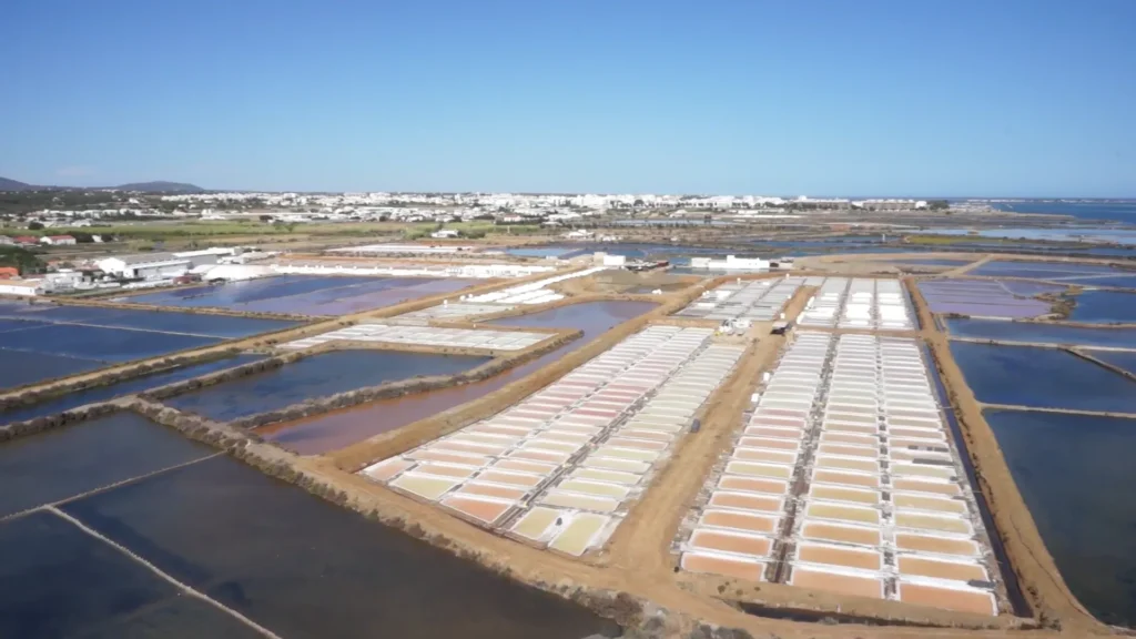 Vue aérienne rapprochée au drone montrant les rangées géométriques de bassins de cristallisation et d'œillets de la saline Necton, révélant le processus de récolte artisanale du sel marin et de la fleur de sel en Algarve.