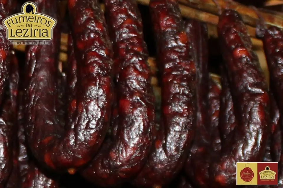 Gros plan sur la texture sombre et dorée de chouriços artisanaux après le fumage au bois de chêne vert chez Quintinha d'Aldeia.