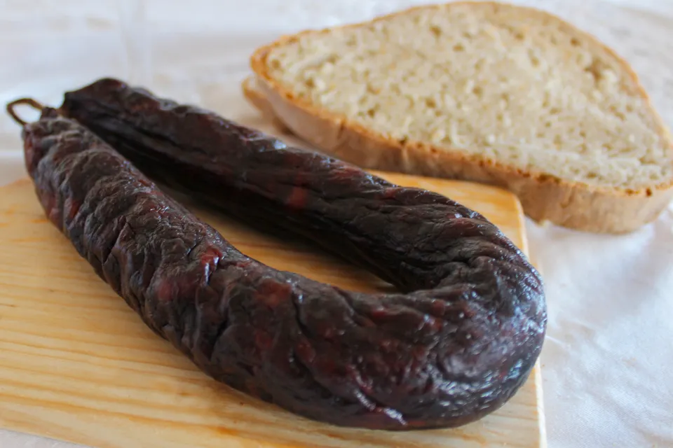 Chouriço Noir Mouro traditionnel de Quintinha d'Aldeia présenté sur une planche en bois à côté d'une tranche de pain rustique.