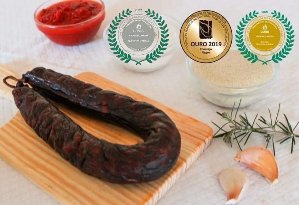 Chouriço Noir Mouro artisanal de Quintinha d'Aldeia sur une planche en bois entouré d'ingrédients et affichant ses médailles de concours (Argent 2022, Or 2019, Or 2020).