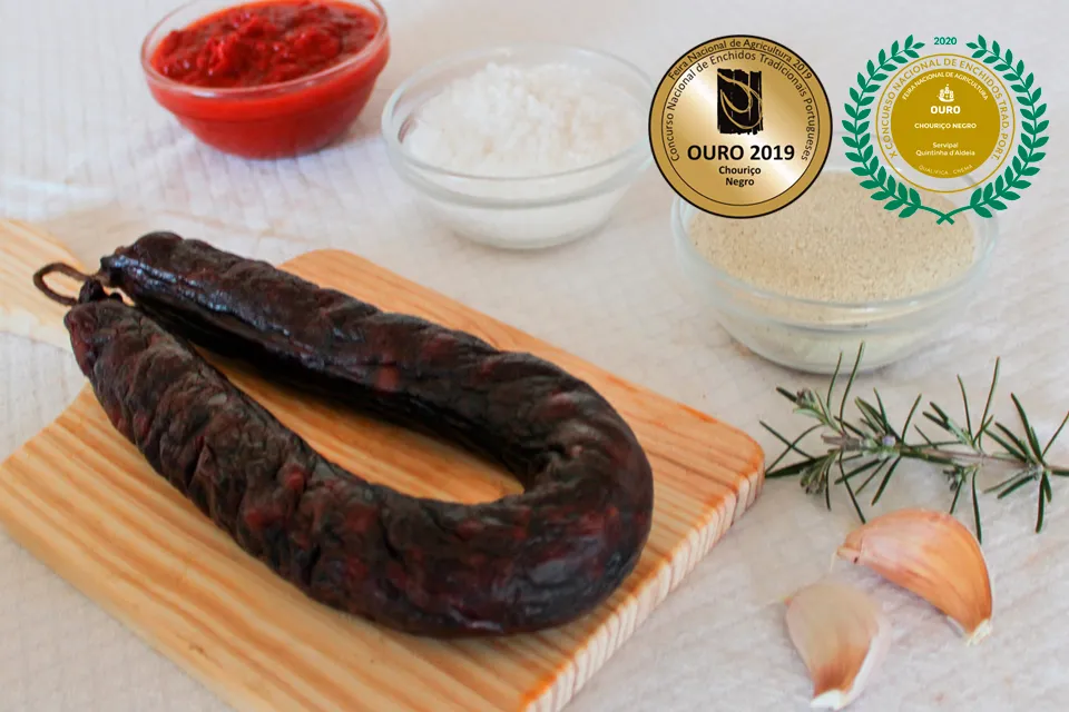 Chouriço Noir Mouro artisanal de Quintinha d'Aldeia sur une planche en bois avec ingrédients et médailles d'Or 2019 et 2020 du concours national d'enchidos.