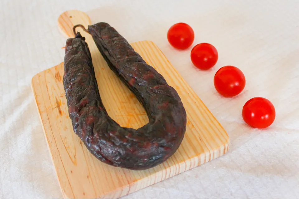 Chouriço Noir Mouro traditionnel de Quintinha d'Aldeia présenté sur une planche en bois avec quatre tomates cerises alignées.