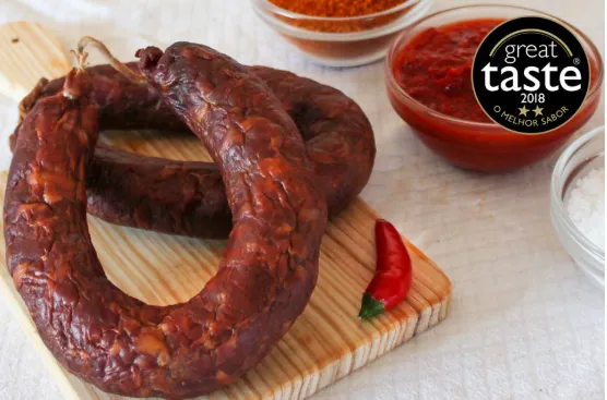 Saucissons fumés Chouriço de Touro Bravo chorizo de taureau brave traditionnel sur planche en bois avec le macaron Great Taste et coupelles d'épices.