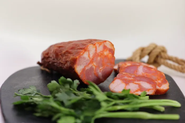 Painho saucisson sec fumé portugais entamé et coupé en tranches de Quintinha d'Aldeia présenté sur un plateau noir avec des brins de persil frais.