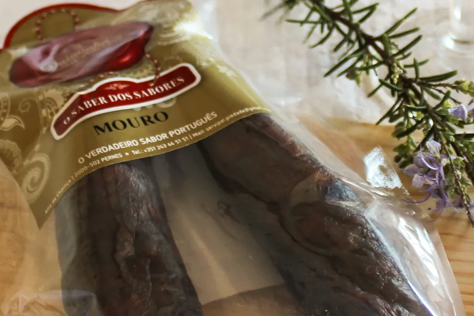 Gros plan sur le sachet emballé sous vide du Chouriço Noir Mouro traditionnel de Quintinha d'Aldeia à côté d'une branche de romarin.
